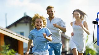 Vater, Mutter und Kind laufen glücklich durch Wiese 