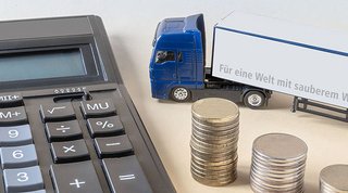 Taschenrechner, Münzen und ein LKW-Miniaturmodell mit ATB Logo auf Tisch platziert